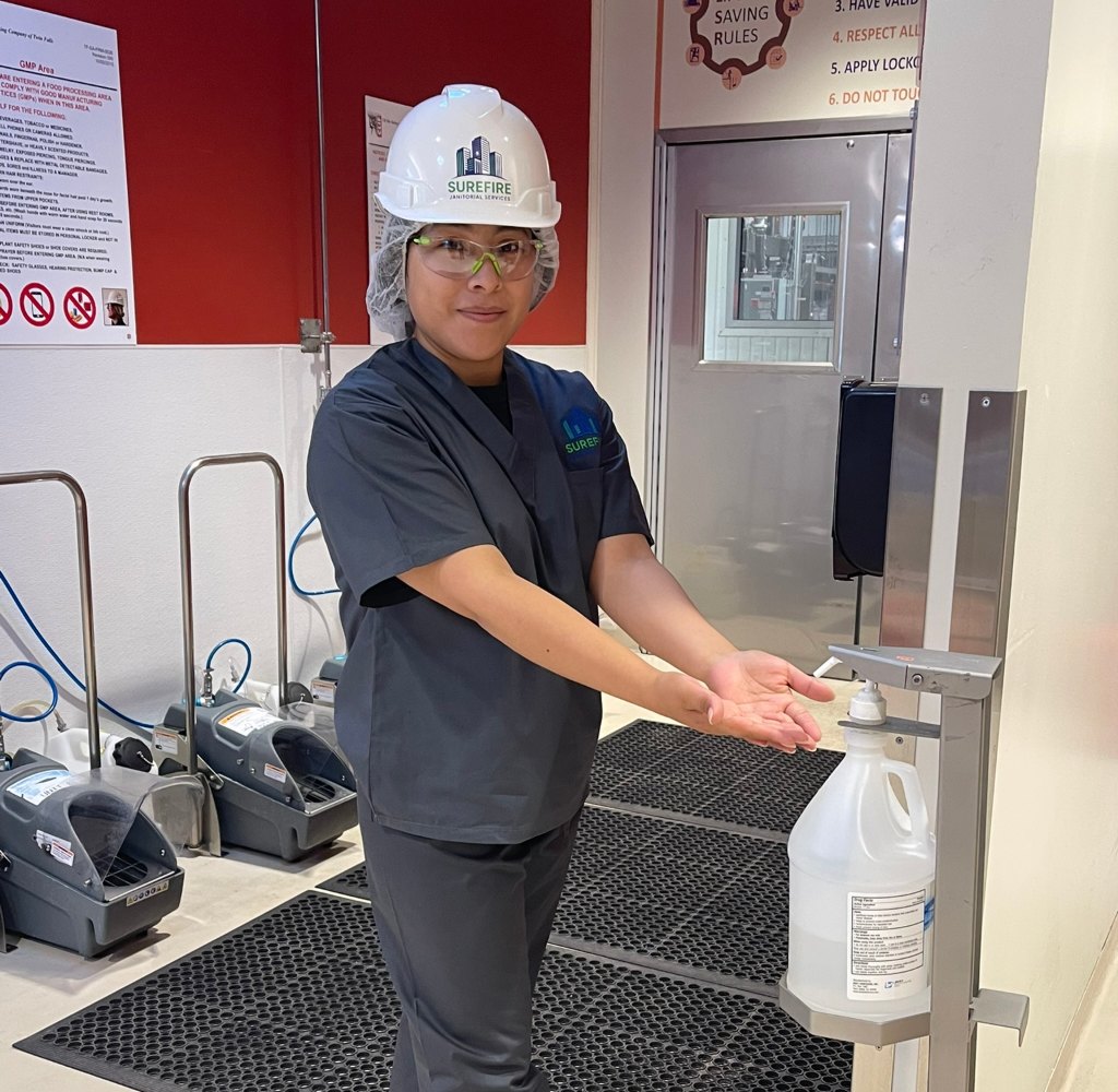 Surefire Janitorial Services team member in hard hat and hairnet at a GMP hand sanitizing station